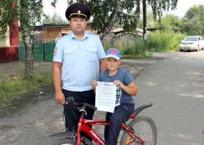 Лейтенант полиции, участковый оперуполномоченный Евгений Васильев вручает памятку юному  велосипедисту.  